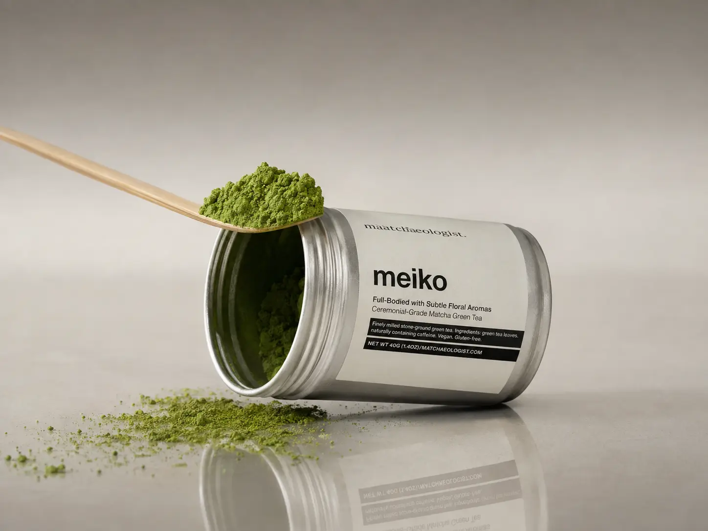 Meiko matcha tin and bamboo scoop staged in a clean reflective product composition
